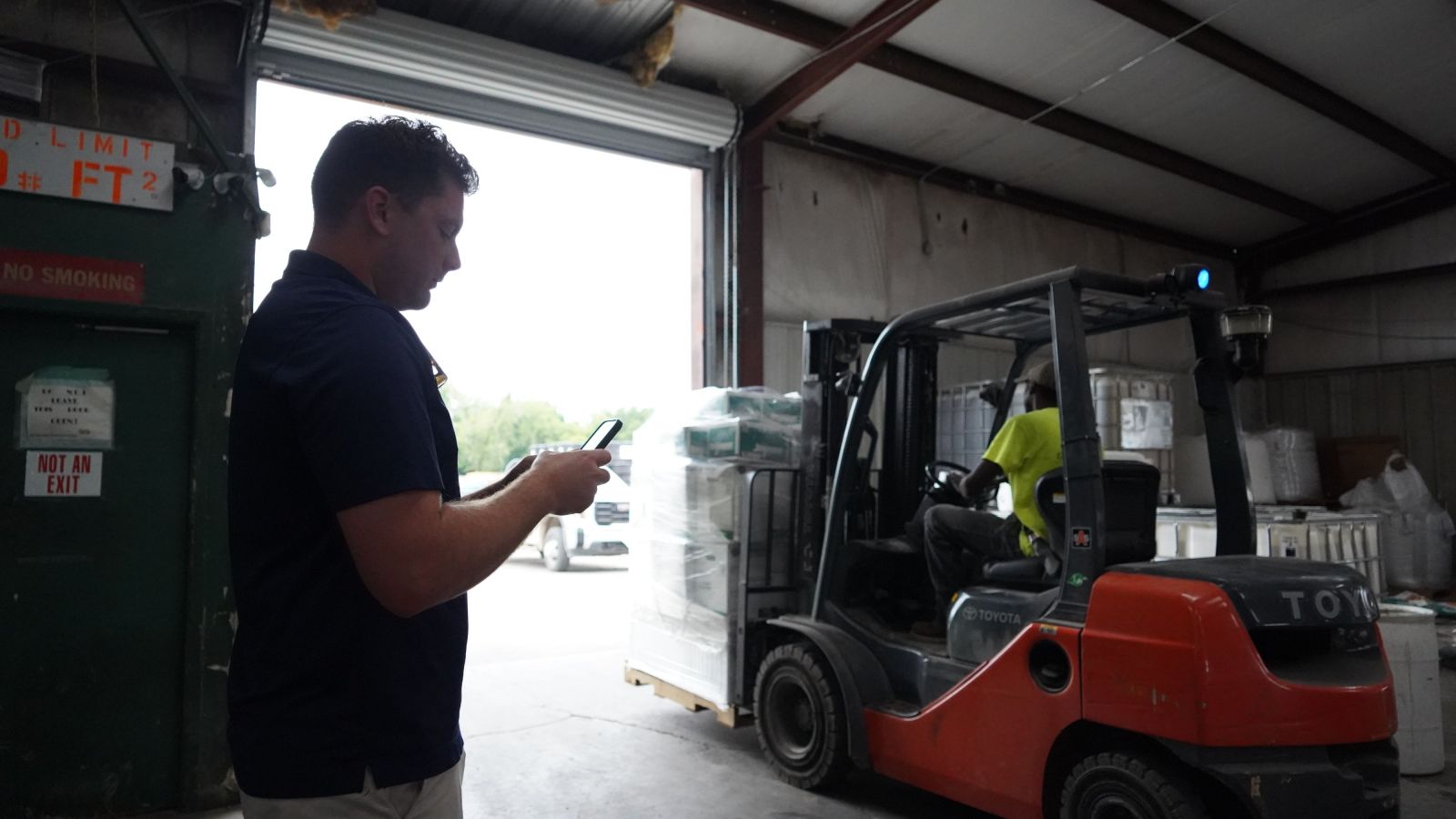Employee on Phone in Warehouse and Employee on Forklift in Background