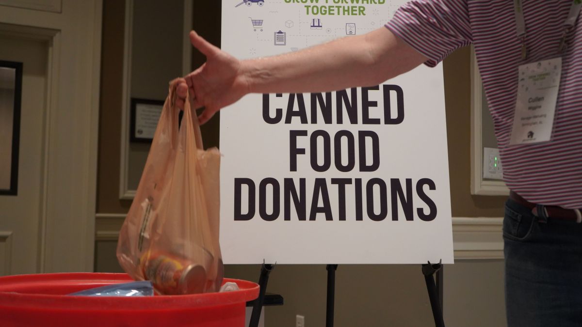 Canned Food Donation Sign with Team Member Dropping Canned Goods in Donation Bin